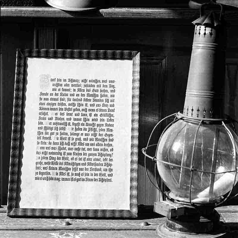 Nahaufnahme einer historischen Komposition in Haus Doorn, fotografiert von Peter Bock-Schroeder (1960). Links steht ein gerahmter, in Frakturschrift gedruckter Text mit lebensphilosophischen Betrachtungen über Schmerz, Zufriedenheit und göttliche Fügung.