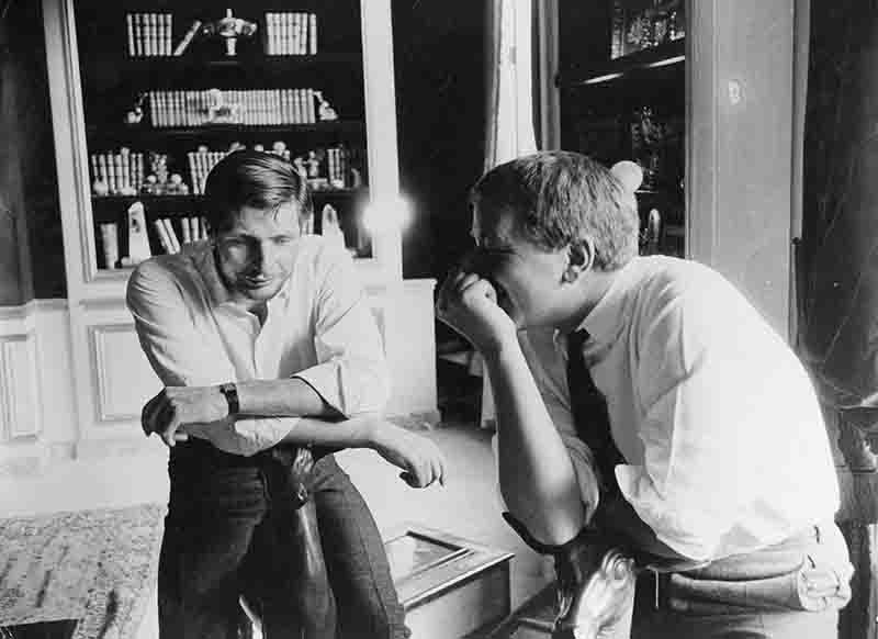 Historische Schwarz-Weiß-Fotografie von Gunter Sachs und Peter Bock-Schroeder in einem eleganten Interieur mit Bücherregalen. Die Aufnahme fängt einen informellen Moment der Verbindung zwischen den beiden Männern ein und dient als Beispiel für hochwertige Vintage-Fotografie auf dem Sekundärmarkt.