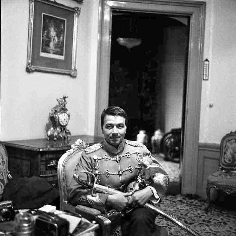 Ein Schwarz-Weiß-Selbstporträt des Fotografen Peter Bock-Schroeder aus dem Jahr 1960 in Haus Doorn. Er sitzt in einem verzierten Sessel und trägt eine historische, reich mit Ornamenten und Epauletten verzierte Uniform von Kaiser Wilhelm II.